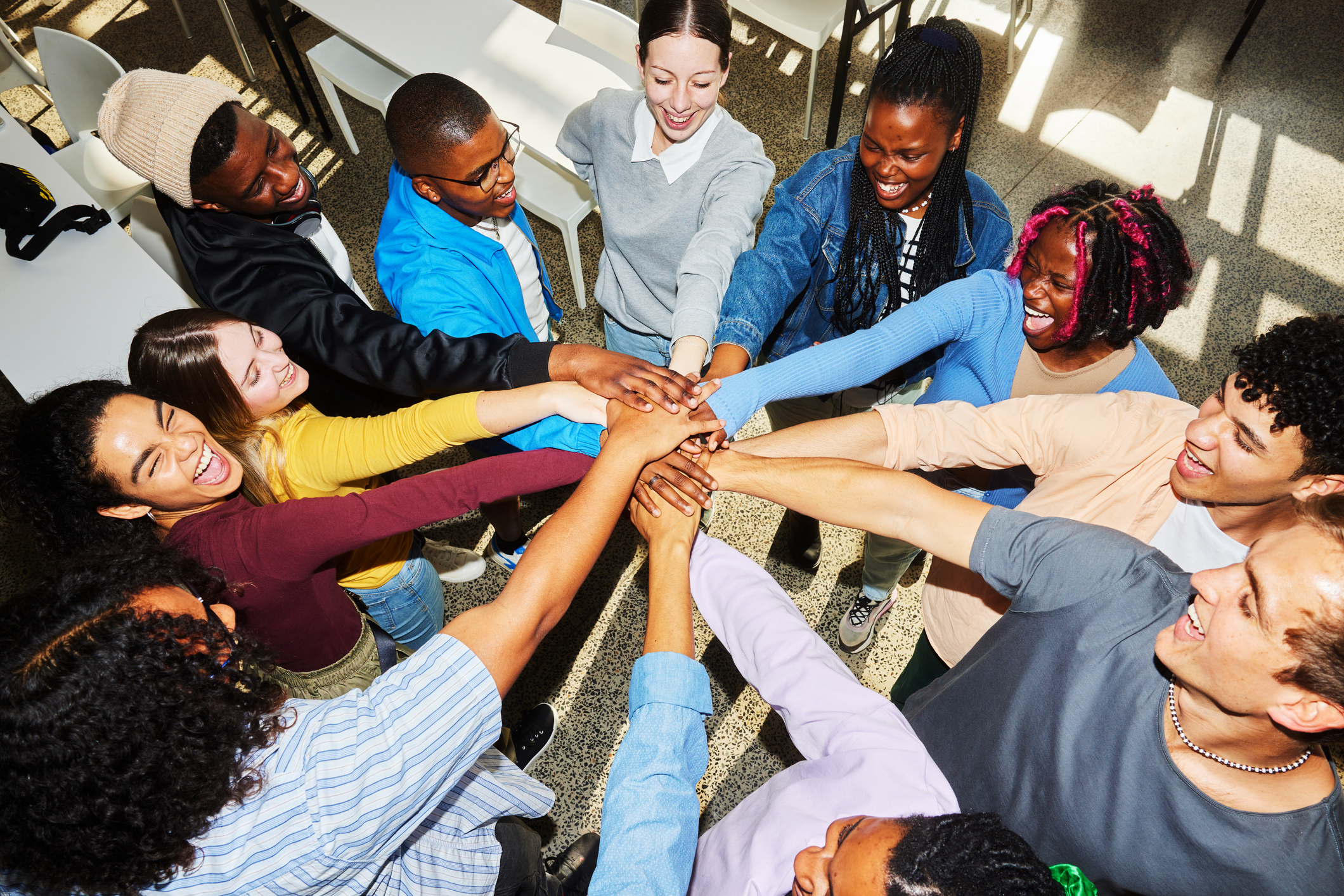 High angle view of a diverse group of smiling young college students standing in a huddle with their hands in a stack between classes at school