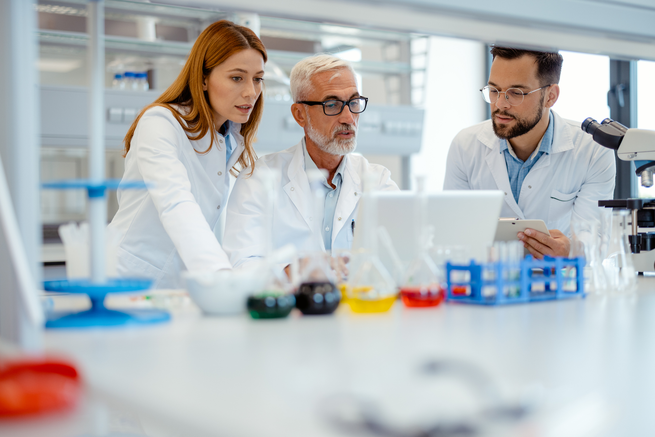 Group of male and female lab technicians and scientists working in laboratory together, doing professional medical research, using laptop, looking at scientific data report, discussing analysis result